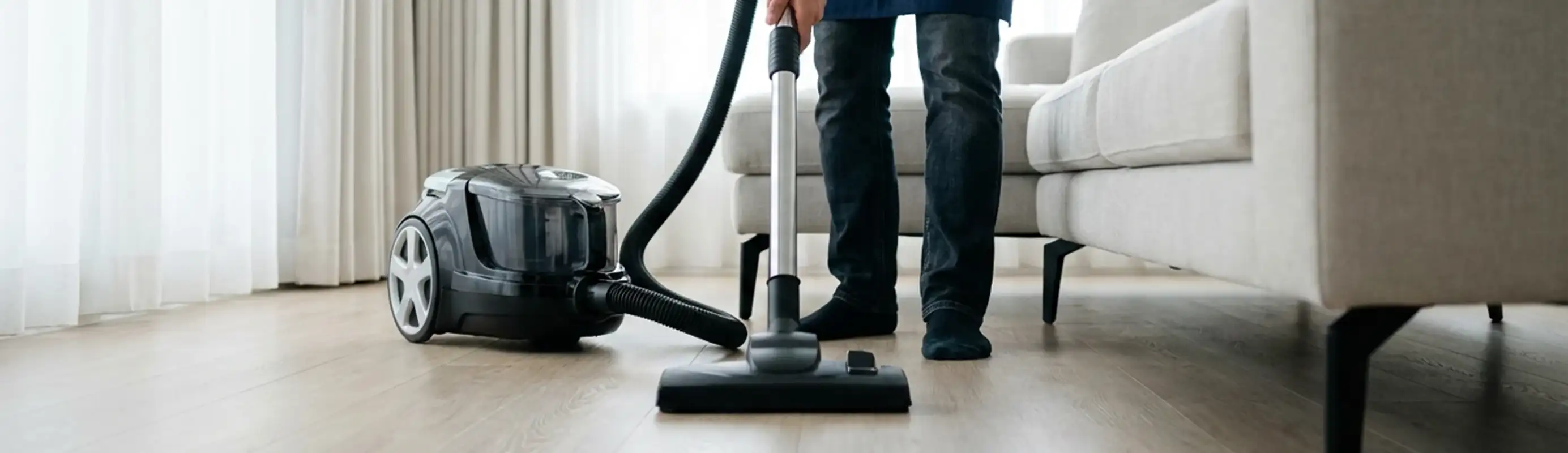 Professional house cleaner vacuuming a living room floor with a canister vacuum cleaner, Ann Arbor, MI.