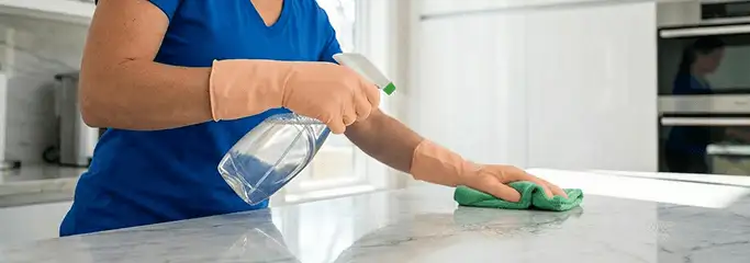 Maid service worker spraying and wiping a kitchen countertop with a microfiber cloth for sanitizing, Ann Arbor, MI.