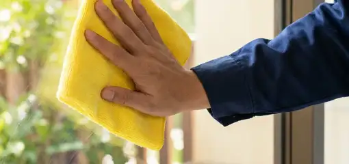 House cleaner wiping a glass window with a yellow microfiber cloth for streak-free cleaning, Ann Arbor, MI.